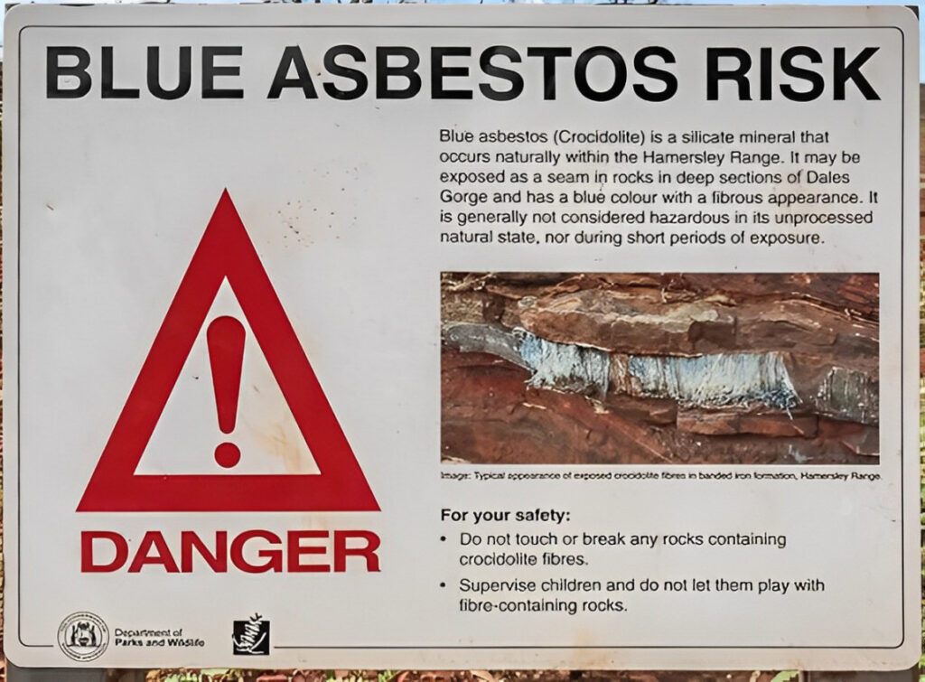 White sign reading "Blue Asbestos Risk" warning of the danger associated with blue asbestos which can be found in the surroundings of the sign. The signs contains a danger icon in red and a photo of how the blue asbestos looks like. This asbestos could be subjected to a Raman Asbestos fiber analysis.



